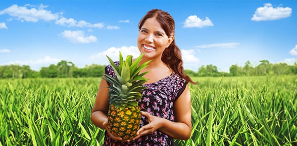 Smiling woman holding a fresh pineapple, highlighting vibrant tropical produce.