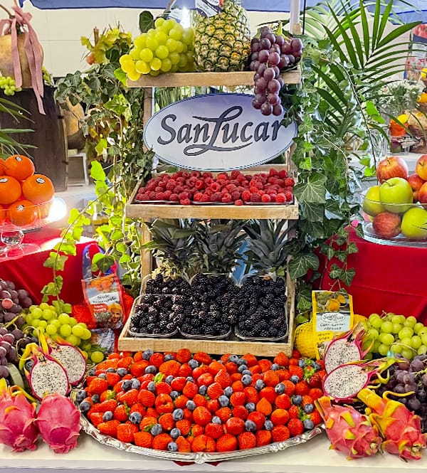 fruta-mix A vibrant SanLucar fruit display featuring fresh strawberries, raspberries, blackberries, grapes, dragon fruit, and pineapples, beautifully arranged with a decorative sign.