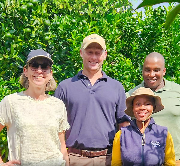 limeten_f Team of farmers standing in front of lush lime trees, smiling under the bright sunlight.