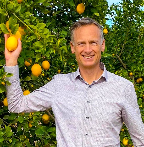 Smiling man in a lemon orchard with bright yellow lemons, showcasing premium citrus produce.