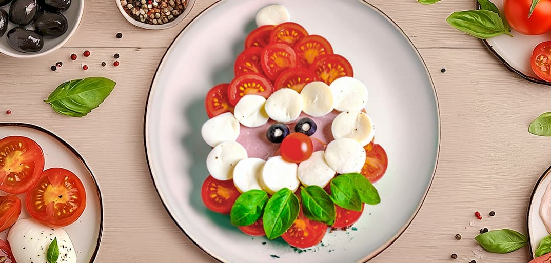 Caprese salad shaped like Santa Claus made with tomatoes, mozzarella, olives, basil, and ham, with a festive setup